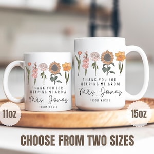 Może przedstawiać: Dwa białe ceramiczne kubki z kwiatowym wzorem i tekstem "Dziękuję za pomoc w rozwoju Pani Jones od Rosie". Kubek po lewej stronie ma pojemność 11oz, a kubek po prawej stronie 15oz.