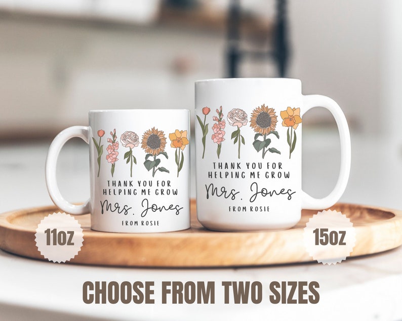 Może przedstawiać: Dwa białe ceramiczne kubki z kwiatowym wzorem i tekstem "Dziękuję za pomoc w rozwoju Pani Jones od Rosie". Kubek po lewej stronie ma pojemność 11oz, a kubek po prawej stronie 15oz.