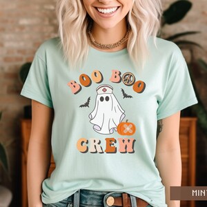 May include: A light blue t-shirt with a ghost wearing a nurse's hat and the text "Boo Boo Crew" in a retro font. The ghost is holding a pumpkin with a bandage on it.