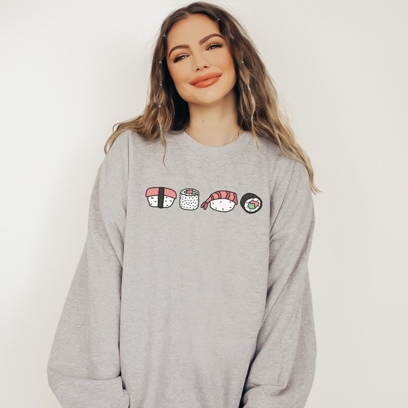 May include: A gray sweatshirt with a graphic of five different sushi rolls. The rolls are drawn in a cartoon style and include salmon, shrimp, and avocado.