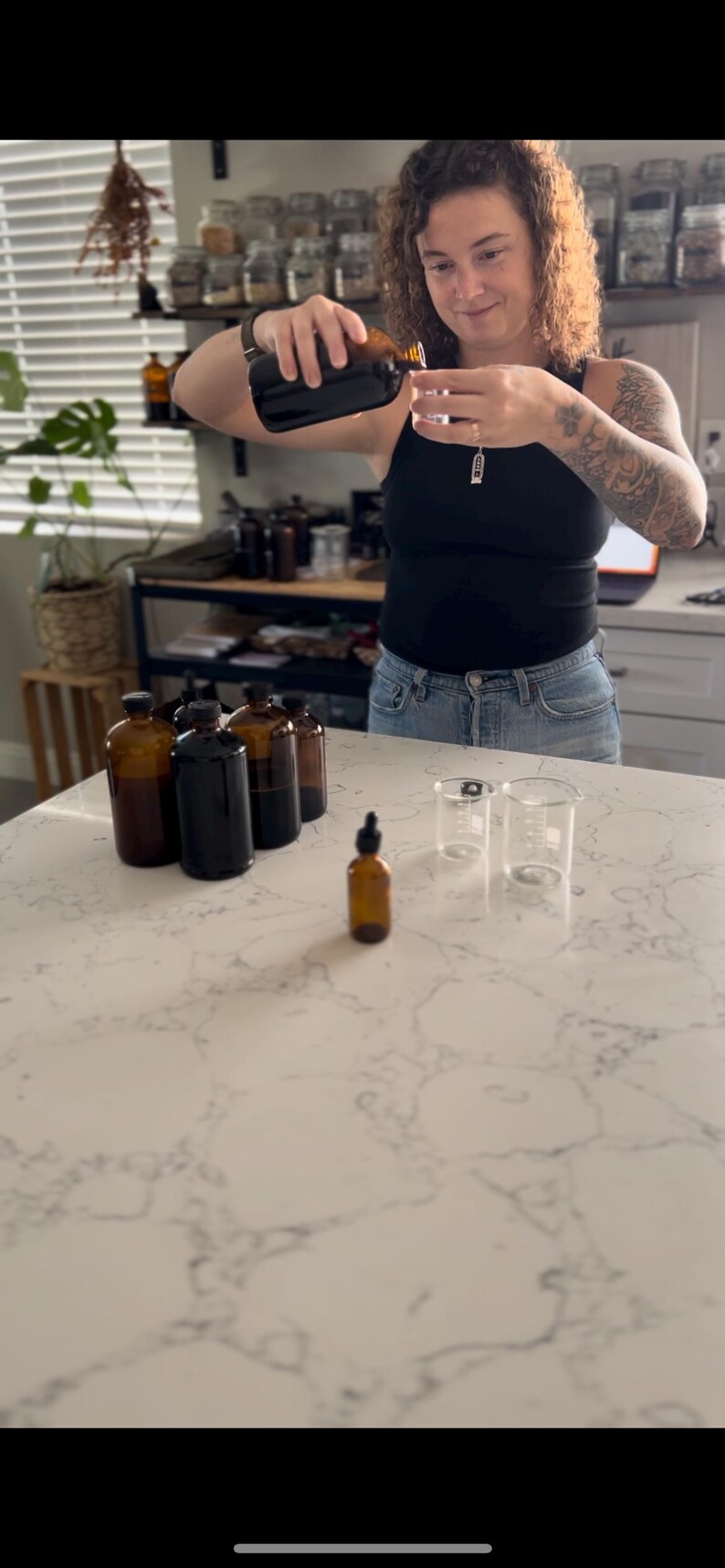 May include: A person pouring liquid from a brown glass bottle into a small glass beaker. Several brown glass bottles and a dropper bottle are on the counter. The scene suggests a laboratory or apothecary setting.