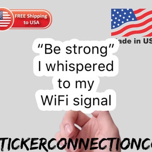 May include: A white sticker with black text that reads "Be strong" I whispered to my WiFi signal. The sticker is on a hand with a gray background. The sticker is made in the USA.