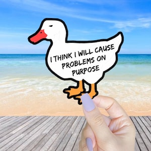 May include: A white cartoon duck with orange feet and a red beak. The duck is holding a sign that says "I think I will cause problems on purpose".