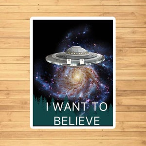 May include: A sticker with a black and silver UFO flying over a galaxy with the text "I WANT TO BELIEVE" in white letters on a teal background.