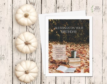 May include: A white card with the text "Blessings on your Birthday" and a quote from Isaiah 58:11. The background image is a pile of autumn leaves with a cup of coffee and a stack of books.