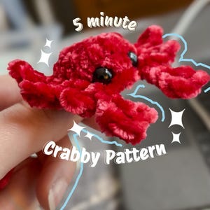 May include: A handmade red plush crab toy with black eyes and multiple legs. The text "5 minute Crabby Pattern" is written on the image. The crab is a soft, fuzzy texture.