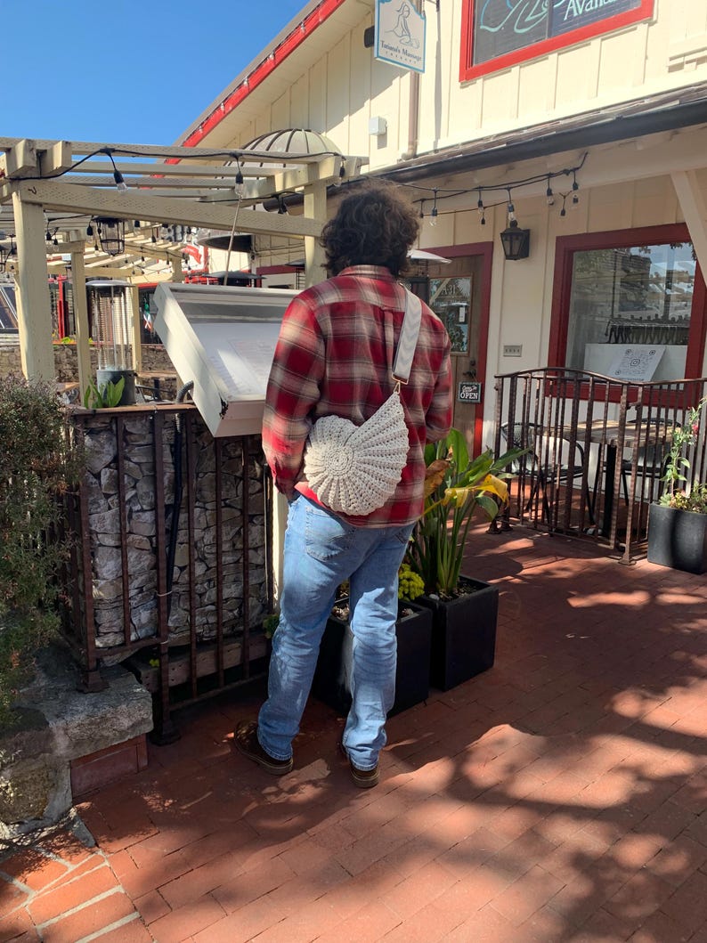 Peut inclure: Une personne portant une chemise &agrave; carreaux rouge et noir et un jean bleu, portant un sac en crochet blanc avec une sangle cr&egrave;me. Le sac a un design en forme d'&eacute;ventail. La personne est &agrave; l'ext&eacute;rieur d'un b&acirc;timent avec une enseigne.