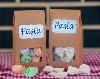 May include: Two brown paper bags with the word "Pasta" printed on them. One bag contains felt pasta shapes, the other contains felt bowtie pasta shapes.