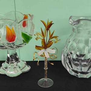 May include: Three clear glass decorative items. A bowl with a floral design, a jug with a textured surface, and a flower-shaped sculpture on a stand.