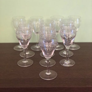 Könnte beinhalten: Ein Set aus zehn klaren Weingläsern mit Stiel und geätzten Designs. Die Gläser sind in einem Kreis auf einer dunkelbraunen Oberfläche angeordnet.