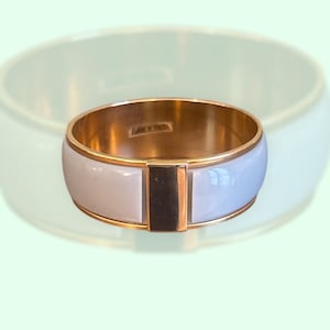 May include: A gold bangle bracelet with a white enamel inlay. The inlay has a gold bar in the centre.