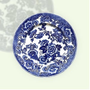 Può includere: Un piatto rotondo in ceramica bianca con un motivo floreale blu. Il piatto presenta un design dettagliato di fiori, foglie e bordi decorativi. La combinazione di colori blu e bianco conferisce al piatto un'estetica classica e vintage.