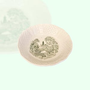 Puede incluir: Un tazón de cerámica blanco con un diseño verde y blanco de un edificio y árboles. El tazón tiene una superficie texturizada.