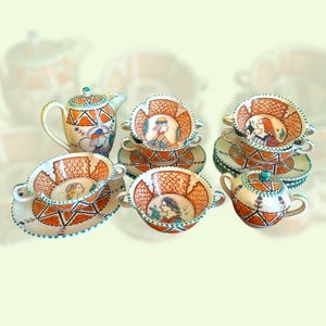 May include: A collection of hand-painted ceramic tableware featuring a teapot, sugar bowl, and several teacups with saucers. The pieces have orange and white geometric patterns and portraits of women. The rims are decorated with a turquoise trim.