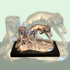 Scultura di cane da caccia che insegue una lepre, realizzata da Ottaviani. La scultura è realizzata in resina ricoperta in argento e poggia su una base in legno.