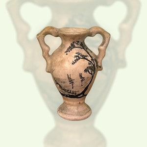 Può includere: Un vaso in ceramica beige con due manici e una scena di paesaggio dipinta in nero. La scena raffigura un albero e barche sull'acqua. Il vaso ha una base rotonda e un'ampia apertura.