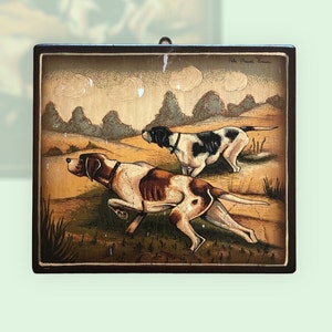 Op de afbeelding: Een houten plaquette met een geschilderd tafereel van twee honden die over een veld rennen. De honden zijn bruin en wit, en het veld is groen met bruine bomen op de achtergrond. De plaquette heeft een bruin frame en de tekst "Arte Nuova Torino" in de rechterbovenhoek.