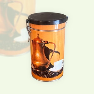 May include: A brown and orange metal canister with a hinged lid and a clasp. The canister has a design of a copper coffee pot, a cup and saucer, and coffee beans.