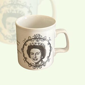 May include: White ceramic mug with a black and white image of Queen Elizabeth II in a crown and ornate frame. The text "To celebrate the Silver Jubilee of Her Majesty Queen Elizabeth II 1977" is printed on the mug.