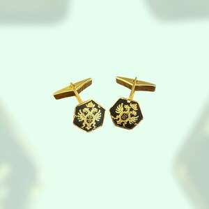 Puede incluir: Un par de gemelos de oro con esmalte negro y un diseño de águila bicéfala de oro.