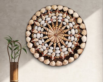 Può includere: Decorazione murale circolare composta da varie conchiglie, disposte in un motivo radiale. Il design presenta una stella centrale di conchiglie allungate, circondata da un mix di conchiglie bianche, beige e marroni. L'opera è montata su uno sfondo scuro e strutturato.
