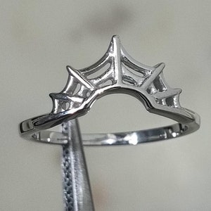 May include: A silver ring with a spiderweb design. The ring is made of metal and has a delicate, intricate design.