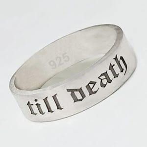 May include: A silver ring with the inscription "till death" in a gothic font. The ring is marked with "925" and has a flat band design. The ring is a piece of jewelry.
