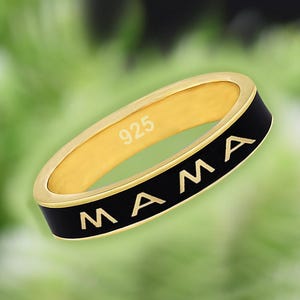 May include: A gold ring with a black enamel band and the word "MAMA" inscribed in gold lettering. The ring is stamped with "925" on the inside.