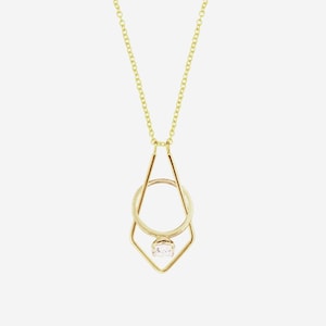 Puede incluir: Un collar de oro con un colgante geométrico que presenta un anillo con una sola piedra transparente.