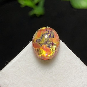 Puede incluir: Un colgante ovalado con un diseño multicolor llamativo. El colgante presenta una mezcla de tonos naranja, amarillo y morado, creando una apariencia única y cautivadora. La superficie tiene un efecto texturizado, casi agrietado, que añade profundidad e interés visual.