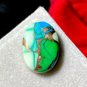 May include: An oval gemstone displaying a mosaic of colours. It features light green, turquoise, and blue shades, with gold-coloured veins. The polished surface reflects light, accentuating the intricate patterns and textures. Ideal for jewellery making, this is a unique piece.