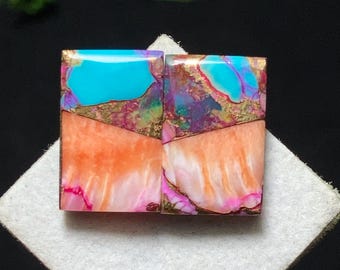 May include: Two rectangular gemstones with a vibrant color palette. The top sections are turquoise, with gold and purple accents. The lower sections are orange and pink, with a marbled appearance. The gemstones are set on a white surface.