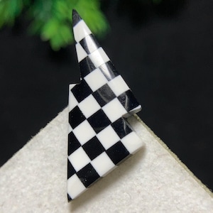 May include: A black and white checkered flag-shaped accessory. The accessory is made of a glossy material and features a classic checkerboard pattern. The design is a bold, geometric shape, perfect for adding a touch of style.