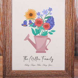 Puede incluir: Una impresión enmarcada con una ilustración de acuarela de una regadera rosa llena de flores coloridas. El texto "The Miller Family" está debajo de la ilustración, con los nombres "Audrey, Harper, Ethan, Henry, Grace" enumerados debajo.