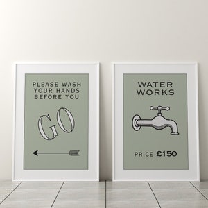 Op de afbeelding: Twee ingelijste kunstprints met een minimalistisch ontwerp. Eén print leest "PLEASE WASH YOUR HANDS BEFORE YOU GO" met een pijl. De andere print toont een kraan en de woorden "WATER WORKS". Beide prints hebben een lichtgroene achtergrond.