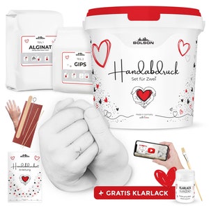 Könnte beinhalten: Ein Handabdruck-Set für zwei Personen, mit weißem Gips, Alginatpulver und einem klaren Versiegelungsmittel. Das Set enthält eine Anleitung und ein Holzwerkzeug zum Glätten des Gipses. Die Verpackung zeigt ein rotes Herzdesign und den Text "Handabdruck Set für Zwei".