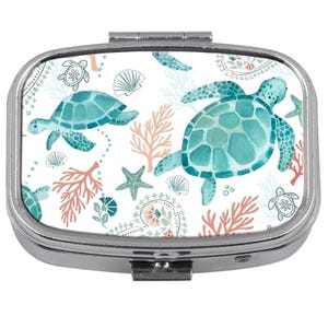 Pode incluir: Uma caixa de comprimidos retangular prateada com tampa articulada. A parte superior apresenta um fundo branco com um padrão de tartarugas marinhas turquesas, corais, conchas e estrelas do mar. As tartarugas têm um efeito aquarela.