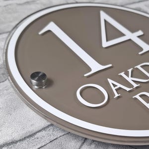 May include: A round address sign with the number "14" in white, set against a taupe background. The sign has a white border and a silver mounting fixture. The text "OAKDALE DR" is also visible.