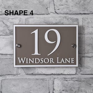 May include: Rectangular house number sign with the number 19 in white, and the words "WINDSOR LANE" below. The sign is brown with a white border and silver mounting hardware. The text "SHAPE 4" is in the top left corner.