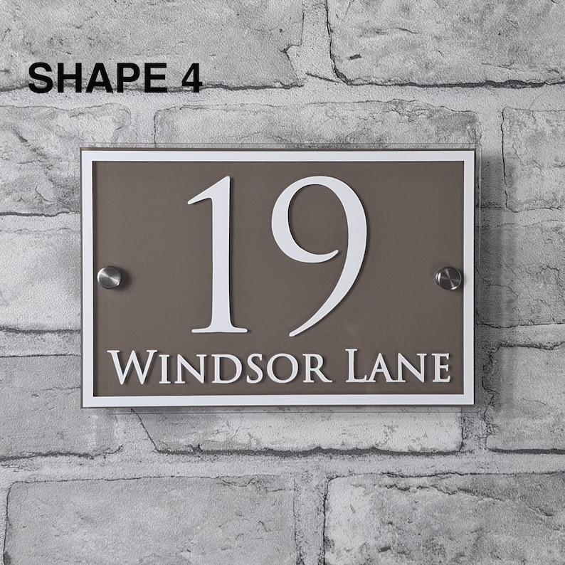 May include: Rectangular house number sign with the number 19 in white, and the words "WINDSOR LANE" below. The sign is brown with a white border and silver mounting hardware. The text "SHAPE 4" is in the top left corner.