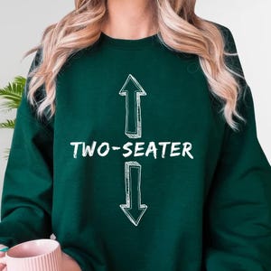 A person wearing a green sweatshirt with the text "TWO-SEATER" printed on it.