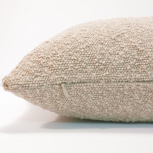May include: A close-up of a beige throw pillow with a zipper closure. The pillow has a textured, woven fabric.