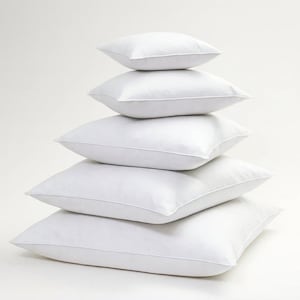 May include: A stack of five white square pillows, each with a piped edge. The pillows are arranged in a pyramid shape, with the largest at the bottom and the smallest at the top. The pillows are clean and fluffy.