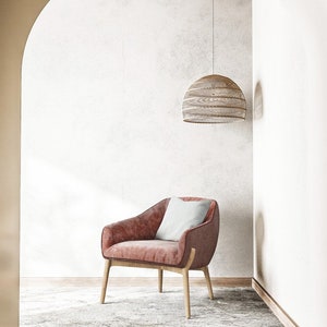 Puede incluir: Un sill&oacute;n rosa con un coj&iacute;n blanco en una habitaci&oacute;n con una pared blanca y una l&aacute;mpara colgante de mimbre colgando del techo.