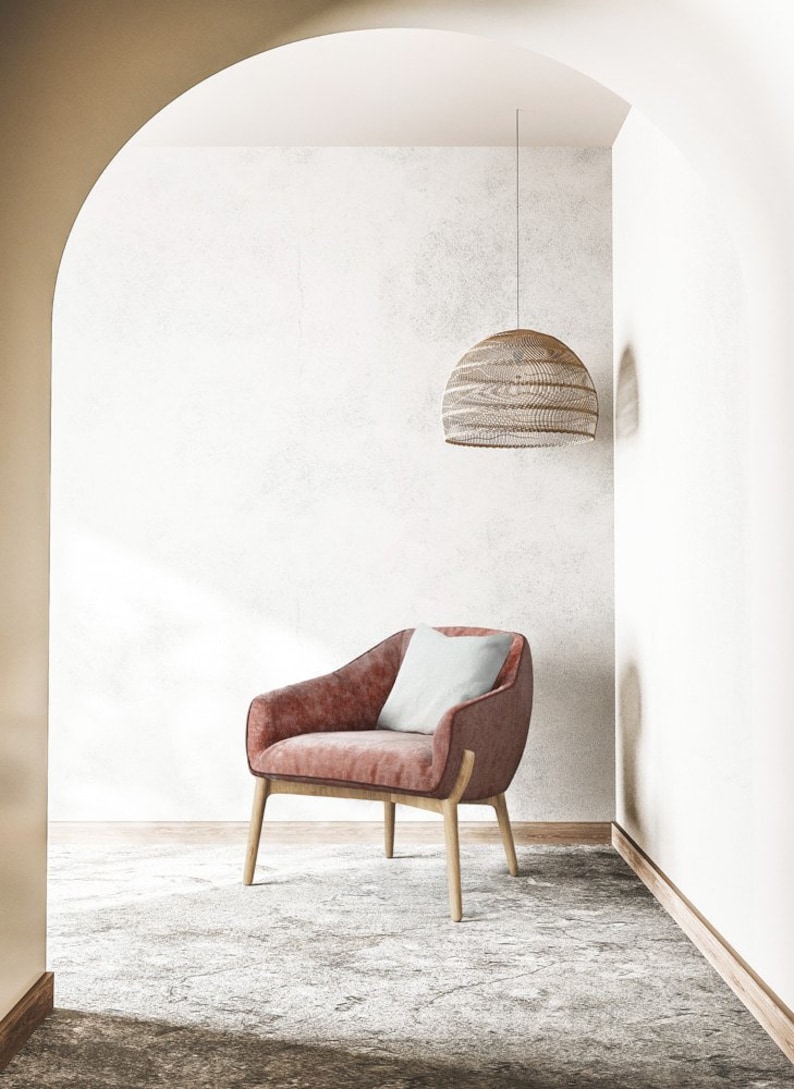 Puede incluir: Un sill&oacute;n rosa con un coj&iacute;n blanco en una habitaci&oacute;n con una pared blanca y una l&aacute;mpara colgante de mimbre colgando del techo.