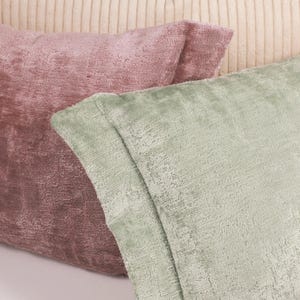 Puede incluir: Dos almohadas decorativas, una de color rosa polvoriento y la otra de color verde salvia. Ambas almohadas tienen una tela texturizada.