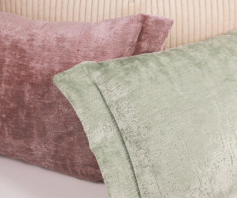 Puede incluir: Dos almohadas decorativas, una de color rosa polvoriento y la otra de color verde salvia. Ambas almohadas tienen una tela texturizada.