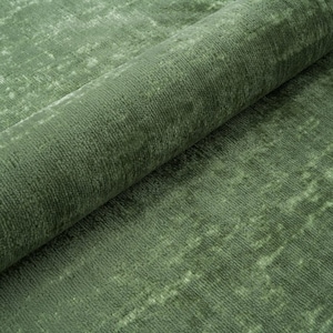 Puede incluir: Primer plano de una alfombra verde con un aspecto texturizado y desgastado. La alfombra est&aacute; doblada por la mitad, mostrando la textura y el color de la tela.
