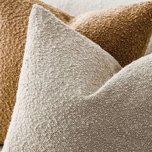 Op de afbeelding: Een set vierkante sierkussens met een sterk getextureerde, noppenachtige bouclé-stof. De kussens worden gepresenteerd in twee verschillende neutrale kleuren, met één kussen in een licht crèmekleurig beige en het andere in een warm goudbruin.