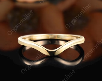 May include: A polished yellow gold ring featuring a V-shaped chevron band. The ring has a smooth, continuous metal surface with a pointed center design that creates a distinct angular silhouette, reflecting light across its curved metallic edges.